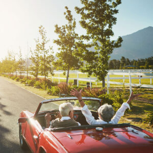 a man and a woman riding in a convertible enjoying a drive on a country road